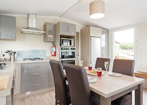 A modern kitchen with a dining area, including a table with chairs, a gas stove, oven, microwave, and a view of the outdoors.