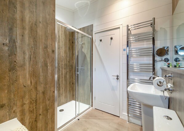 A modern bathroom with a glass-enclosed shower, a white sink, and a chrome towel rack.