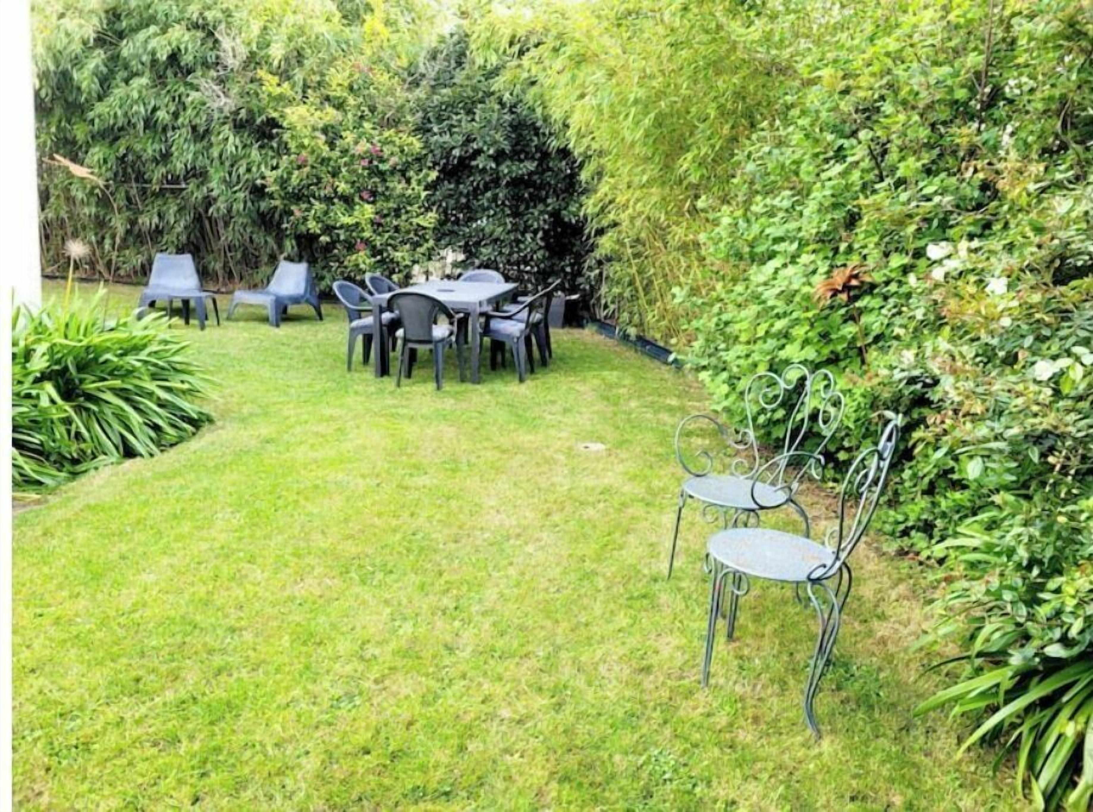Eine Terrasse mit Tisch und Stühlen, umgeben von üppigem Grün und einem Hecken.