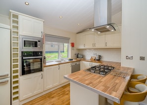 A modern kitchen with white cabinetry, a built-in oven, a gas stove, and a window overlooking a garden.