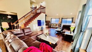 A spacious living room with a large brown leather sofa, a coffee table, and a staircase leading to an upper level. - Amazing Lake View Home w Pool table Ping-Pong BBQ Deck, Watch Sunset  (Kelseyville)