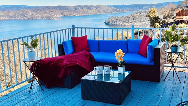 A blue deck with a sofa, red throw blanket, and a coffee table with mugs and flowers. - Amazing Lake View Home w Pool table Ping-Pong BBQ Deck, Watch Sunset  (Kelseyville)