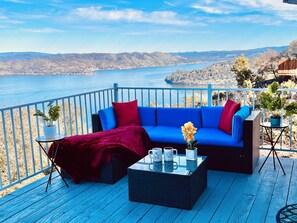 A blue deck with a sofa, red throw blanket, and a coffee table with mugs and flowers.