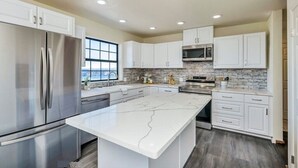 A modern kitchen with white cabinets, a large island, stainless steel appliances, and a brick backsplash. - Amazing Lake View Home w Pool table Ping-Pong BBQ Deck, Watch Sunset  (Kelseyville)