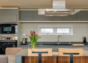 A modern kitchen with grey cabinets, a Bosch range hood, a built-in oven, a coffee maker, a window, and a vase with tulips.