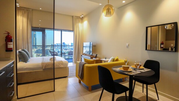 Ein modernes Hotelzimmer mit Bett, einer Couch, einem Esstisch mit Stühlen, Blick auf die Stadt, einem Feuerlöscher und einem Spiegel an der Wand.