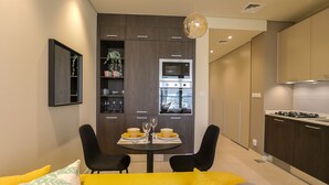 Eine moderne Küche mit integrierten Geräten, ein Essbereich mit gelbem Tisch und schwarzen Stühlen sowie eine Couch mit gelben Kissen.