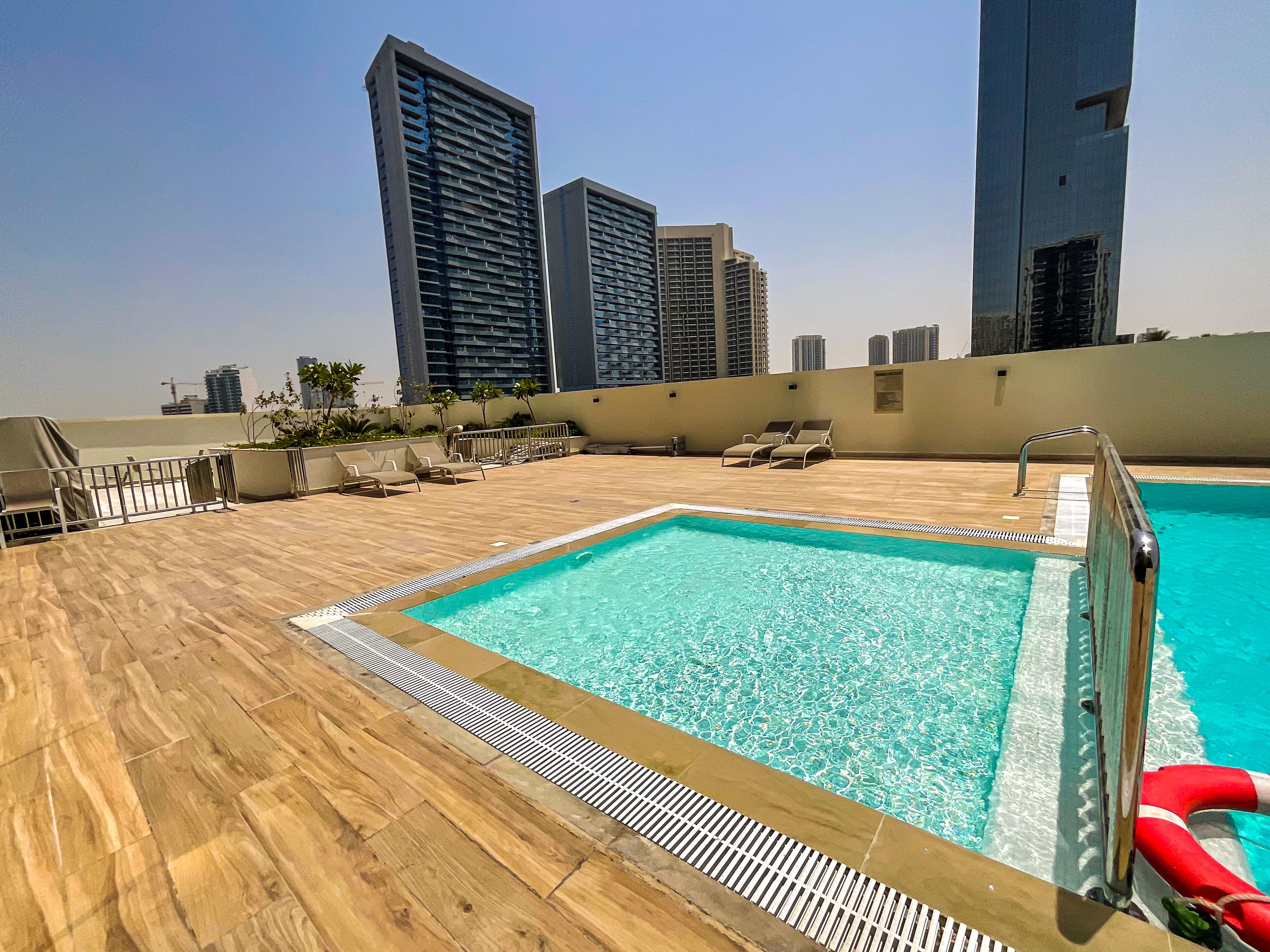 A rooftop pool with a wooden deck, lounge chairs, and a lifeguard stand.