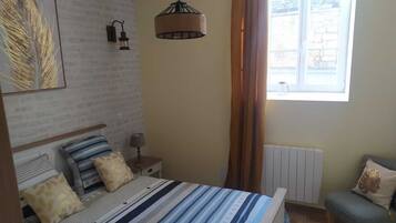 Et soveværelse med seng, sengetøj, lampe og et vindue med gardiner.