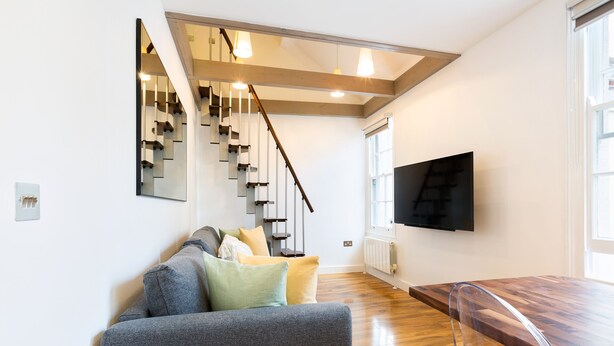 A modern living room with a staircase, a flat-screen TV, and a wooden dining table.