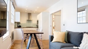 A modern kitchen with a dining table and chairs, a grey sofa with cushions, and a large mirror on the wall.