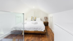 A bedroom with a wooden bed, white bedding, a glass partition, a bedside table with a lamp, and a wooden floor.