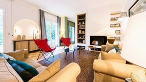 Ein geräumiges Wohnzimmer mit einer großen Sofagarnitur, einem roten Sessel, einem Couchtisch und einem Kamin.