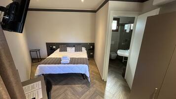 Une chambre d’hôtel avec un lit, un téléviseur fixé au mur, une petite table et un bureau avec une chaise.