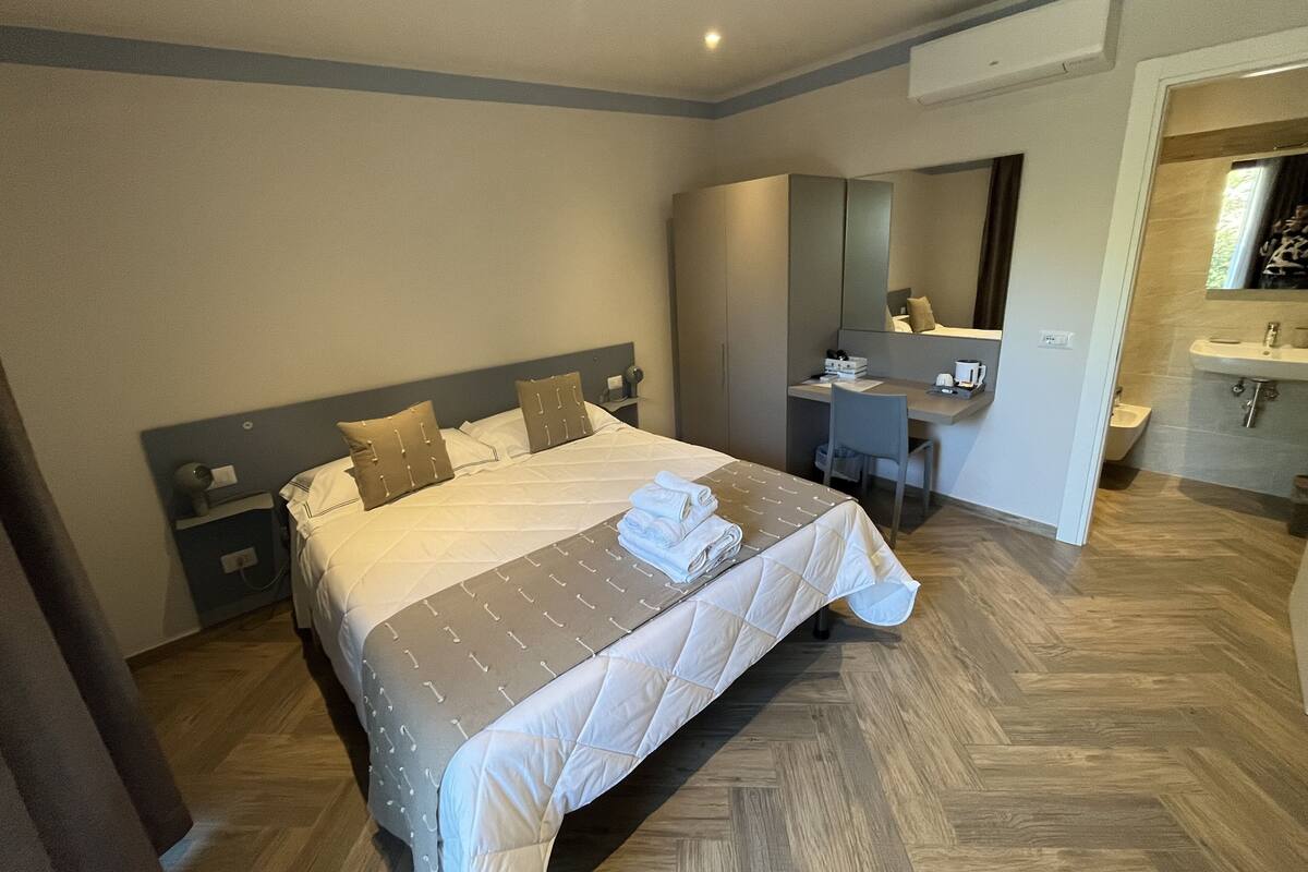 Una habitación de hotel con cama, escritorio, silla, espejo y baño.