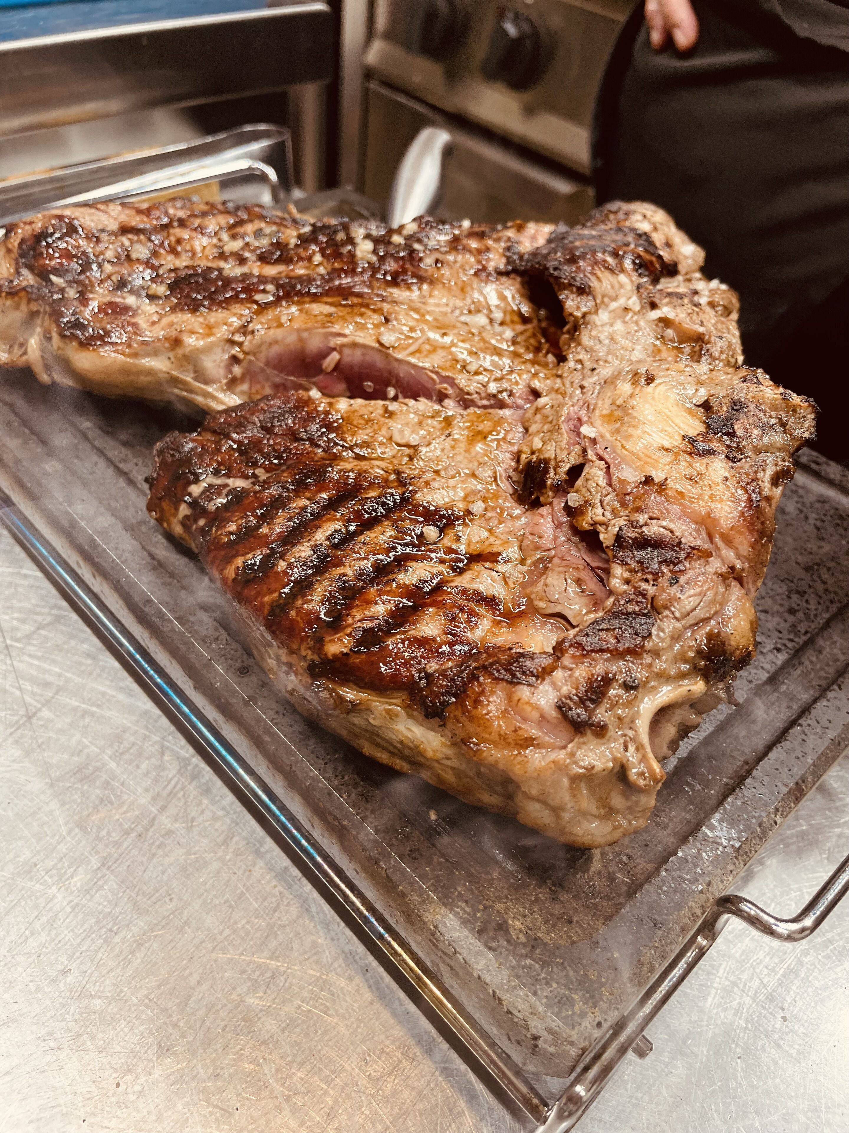 A large, grilled steak on a metal rack in a kitchen.