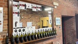 Un mur de briques sur lequel est fixée une étagère à vin présentant différentes bouteilles, un miroir qui reflète le mur et un banc en bois.