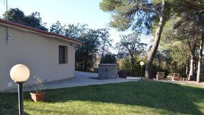 Une maison avec une terrasse dallée, une cheminée en pierre et une pelouse.