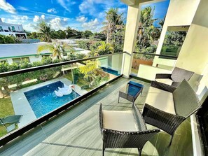 Un balcon doté d’une balustrade en verre, une piscine avec un fauteuil flottant et des meubles en osier.