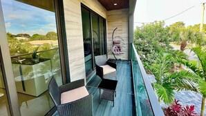 Een balkon met rieten meubels, een hangstoel en uitzicht op groen.