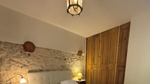 A bedroom with a stone wall, a wooden wardrobe, a bed with white linens, and a nightstand with a lamp. - 5-bedroom Provençal Farmhouse on an organic vineyard (Vacqueyras)