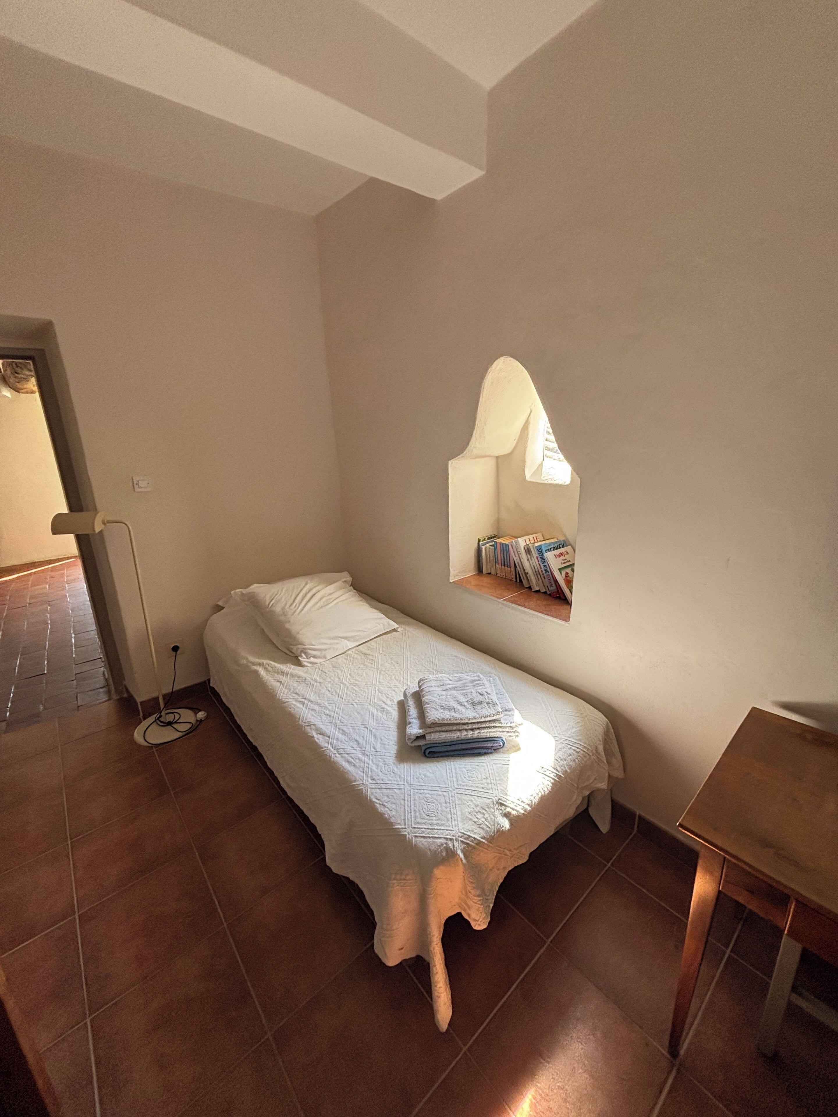 Un dormitorio pequeño y acogedor con una cama individual, una mesita de noche y una estantería en la pared con libros.