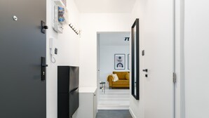 Un couloir étroit, avec un téléviseur à l’écran noir sur le côté gauche, un petit meuble blanc et un canapé jaune au fond.