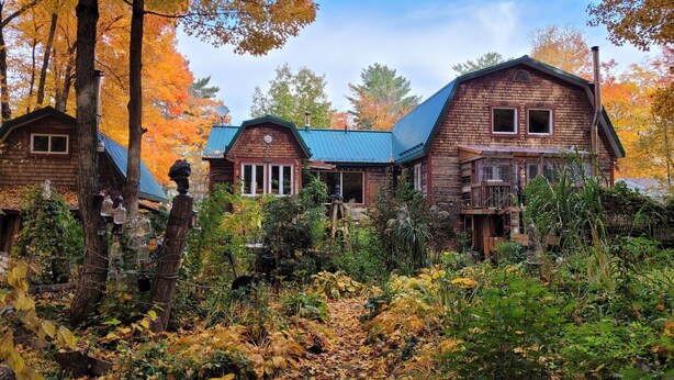 A rustic cabin-style hotel with multiple wooden buildings, surrounded by autumn foliage and a garden. - MA GALÈRE, Eco-responsible house by the river. (Saint-Michel-de-Bellechasse)