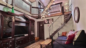 A spacious living room with a wooden staircase, a large TV, and a sofa with colorful cushions. - MA GALÈRE, Eco-responsible house by the river. (Saint-Michel-de-Bellechasse)