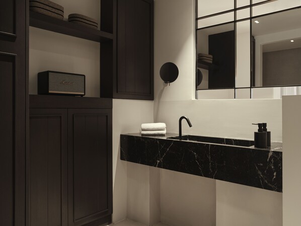 A modern bathroom with dark wood cabinetry, a black marble sink, and a mirror above the sink.