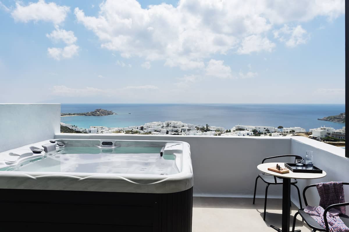 Un balcon avec un jacuzzi, une table et des chaises, et une vue sur la mer et les bâtiments blancs.
