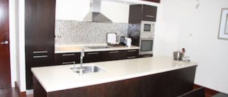 A modern kitchen with dark wood cabinets, a white countertop, and stainless steel appliances.