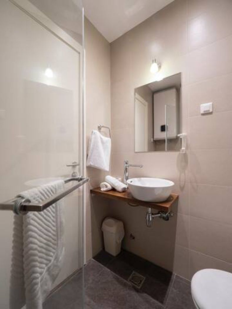 Un baño moderno con cabina de ducha de vidrio, un lavamanos blanco y encimera de madera, y un inodoro.