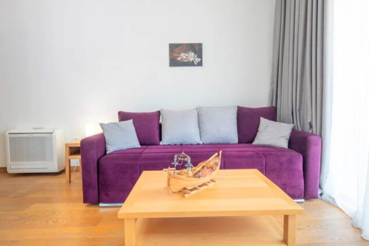 A living room with a purple sofa, a wooden coffee table, and a small ship model.