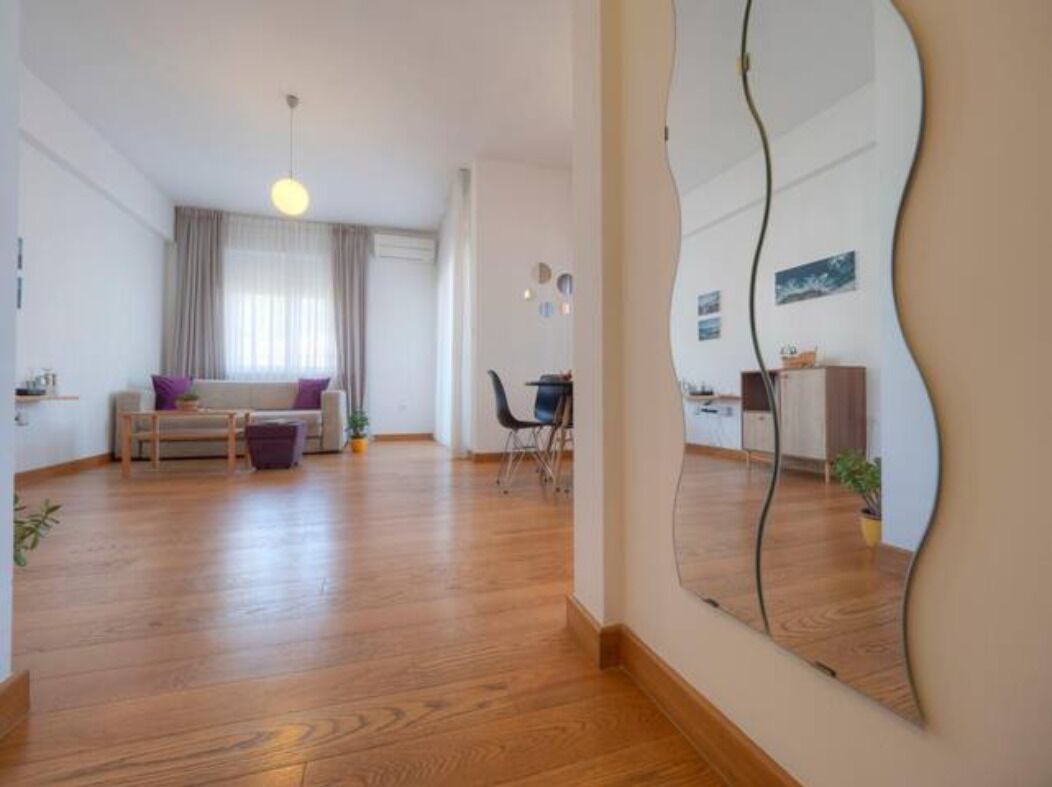 A spacious living area with a sofa, coffee table, and a dining table. A large mirror reflects part of the room.