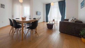 Una sala de estar moderna con comedor, suelo de madera, un sofá y un televisor.