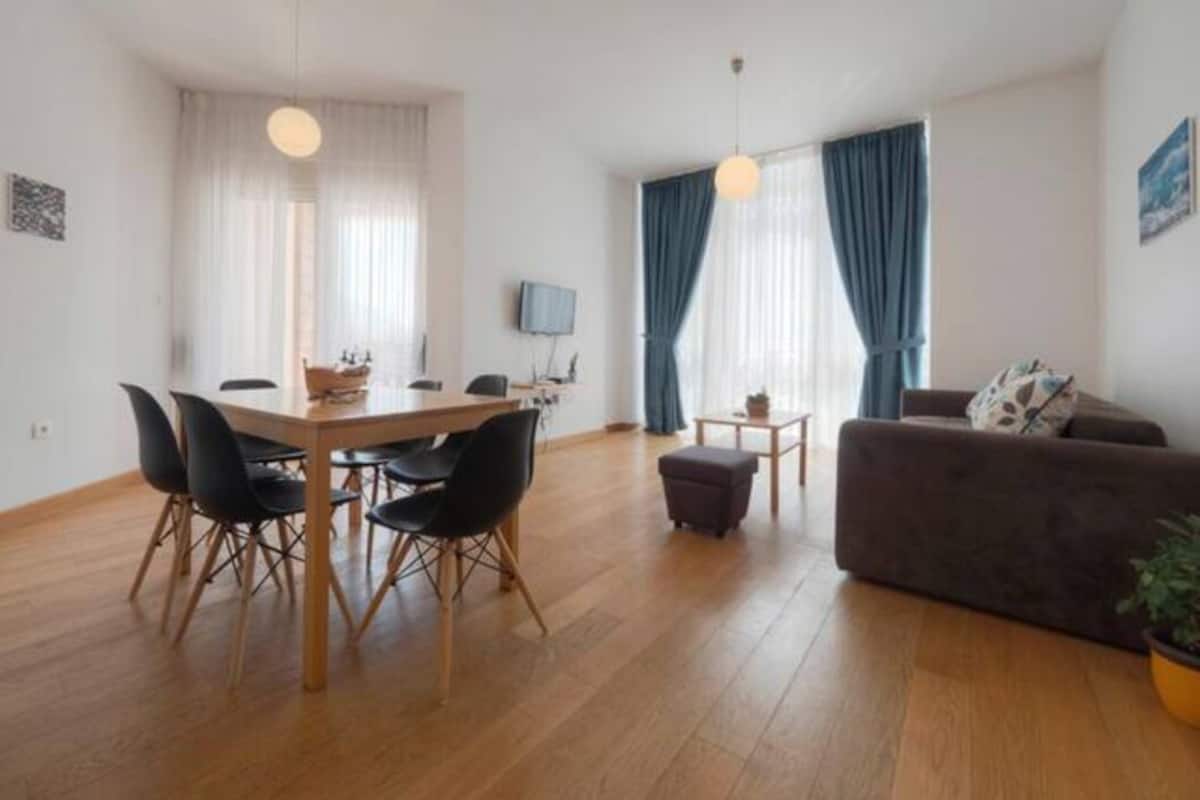 A modern living room with a dining area, wooden flooring, a sofa, and a TV.