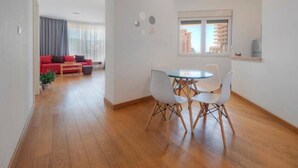 Una sala de estar moderna con un sofá rojo, una mesa de comedor con sillas y un amplio ventanal con vistas a edificios.