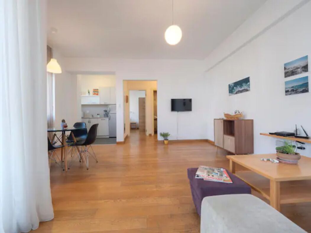 A modern living room with a sofa, a dining table, and a TV mounted on the wall.