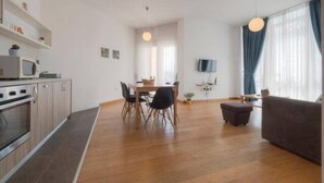Una sala de estar moderna con un sofá, un comedor con mesa y sillas, y una cocina con armarios y electrodomésticos.