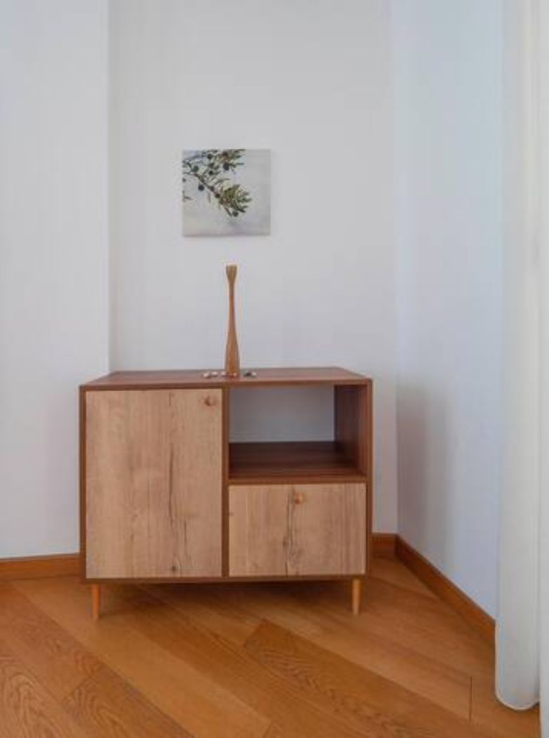 A wooden cabinet with a vase on top, a small shelf, and a framed picture on the wall.