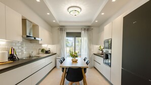 A modern kitchen with a dining table, chairs, a refrigerator, and a window with curtains. - Violet Maison (Kos)