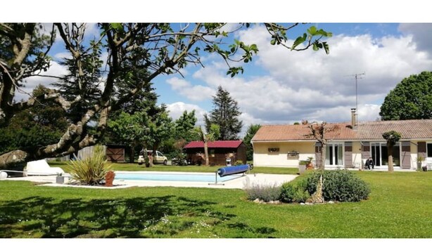 A residential property with a swimming pool, a covered patio, and a large tree in the foreground. - Gîte ave Piscine (Illats)