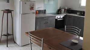 A compact kitchen with a built-in oven, a stove, and a sink. There is a wooden dining table with chairs. - Gîte ave Piscine (Illats)