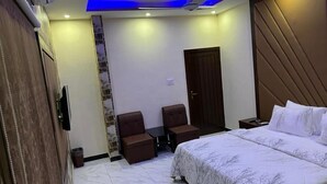 Ein Schlafzimmer mit einem Bett, zwei Stühlen, einem Kleiderschrank, einer Tür und einem Deckenventilator.
