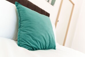 A teal pillow on a white bed in a hotel room.