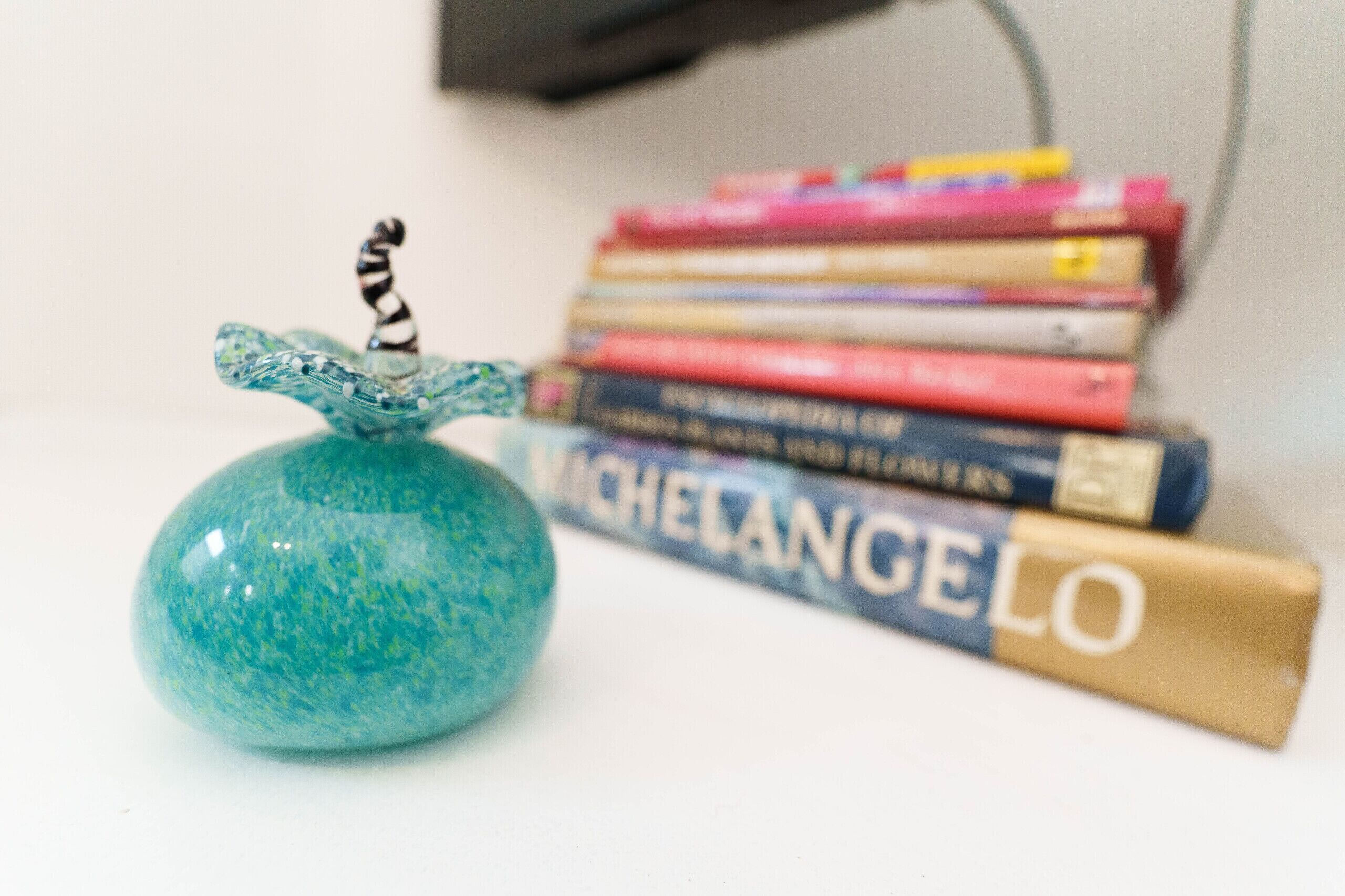 A decorative glass object with a spiral top, placed in front of a stack of books.