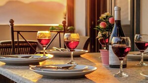 Une table dressée pour un repas, avec des verres à vin, des assiettes, des couverts et une bouteille de vin, et en arrière-plan, une vue sur le coucher de soleil.