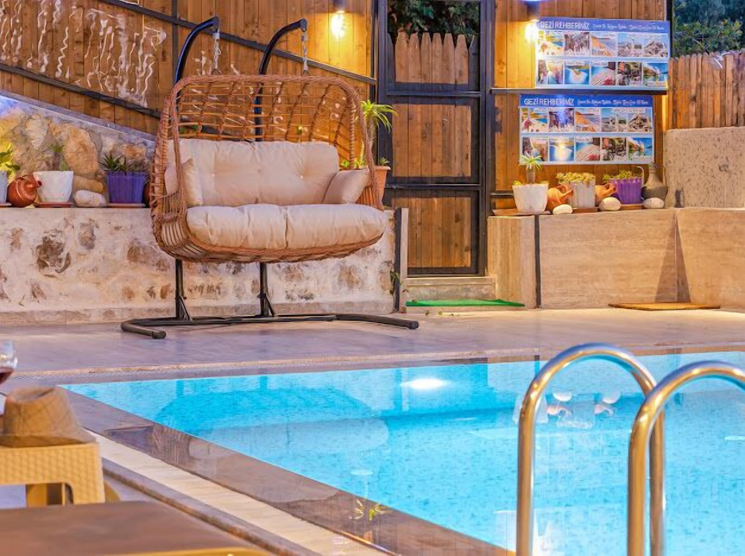 Un espace aménagé au bord de la piscine, avec un fauteuil en osier, un mur en bois orné d’une affiche et un mur en pierre agrémenté de plantes.