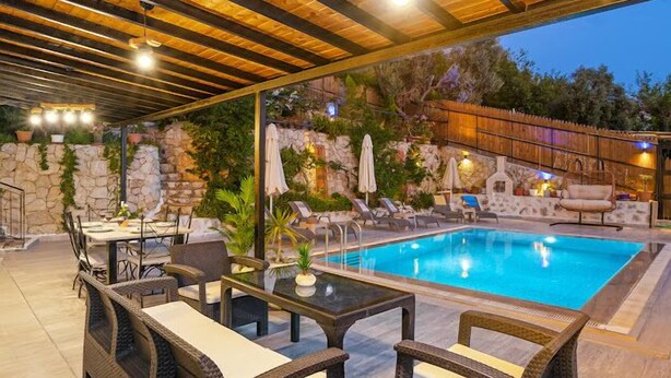 Un espace extérieur avec une piscine, des chaises longues, une table à manger et un mur en pierre en arrière-plan.
